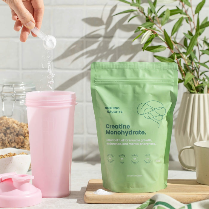 Green package of creatine monohydrate with a pink cup and spoon on a kitchen counter.